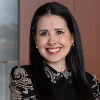 Portrait of Diana McWilliams, smiling and wearing a black patterned blouse, photographed in a modern indoor setting